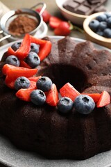 Tasty chocolate bundt cake with berries on table, closeup