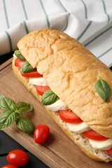Tasty sandwich with mozzarella cheese, tomatoes and basil on black wooden table, closeup