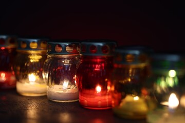 Many grave candles on black table against red background, closeup