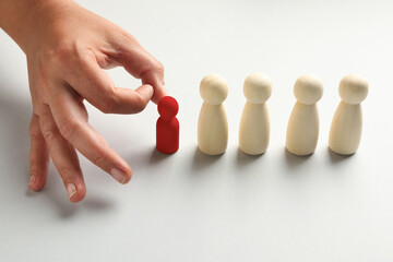 Dismissal. Woman choosing red figure among wooden ones at white table, closeup