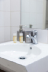 Fototapeta premium Modern bathroom sink with chrome faucet and blurred toiletries