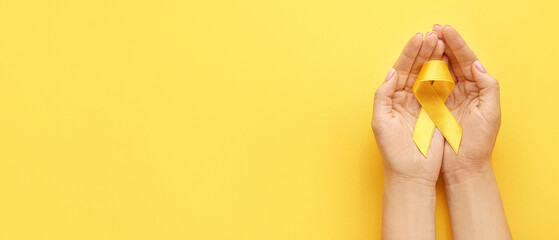 Female hands with yellow ribbon on color background. Cancer awareness concept