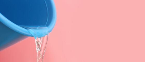Pouring of water from bucket on color background, closeup