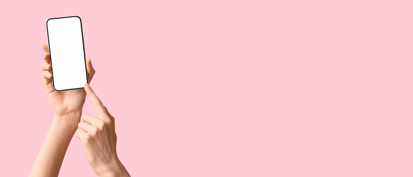 Female hands holding modern mobile phone on pink background, closeup