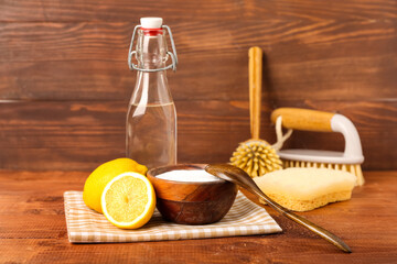 Bowl of baking soda, lemons, vinegar and cleaning supplies on wooden background
