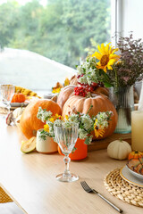 Autumn setting with pumpkins and flowers on dining table in room, closeup