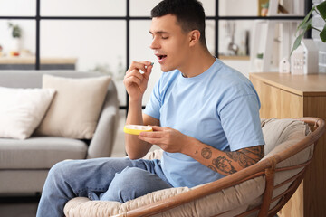 Young man taking pill from pillbox at home