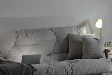 Sofa with pillows and glowing laptop in living room at night
