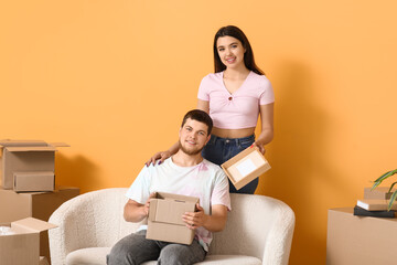 Young happy couple sitting on sofa with belongings near orange wall in their new house