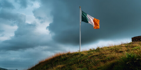Irish flag flagpole grassy hill cloudy sky outdoor windy weather national symbol green white orange landscape nature stormy