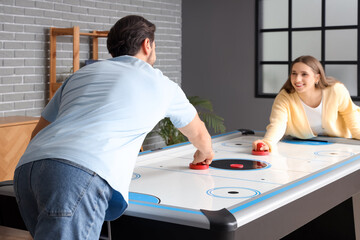 Young woman playing air hockey with her husband at home