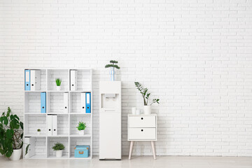 Interior of light office with modern water cooler and shelving unit
