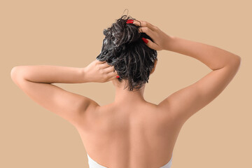 Pretty young Asian woman washing hair on beige background, back view