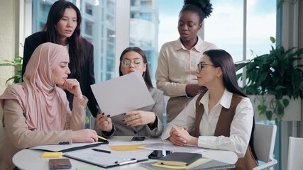 Serious multiethnic women females work team girls African American Japanese Caucasian Arabian Muslim hijab businesswomen analyze document graph low data brainstorm strategy inside office meeting room - Powered by Adobe