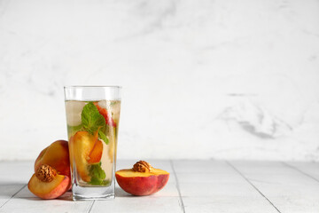 Glass of fresh peach lemonade with mint and fruits on white tile table