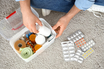 Young man taking pills from first aid kit on carpet at home, top view