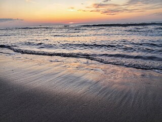 The tranquil beach at sunset, with wet sand reflecting the colorful sky, creates a serene and picturesque coastal landscape in Ustka, Poland.