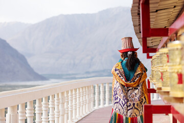 A woman in vibrant traditional attire walks along a monastery corridor in Leh, spinning prayer...