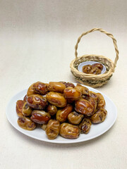 A plate of Khalas dates, ready to enjoy. A small woven basket of dates is in the background.