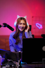 Asian young adult woman playing video game streaming online live broadcasting from home gaming studio with neon lighting setup