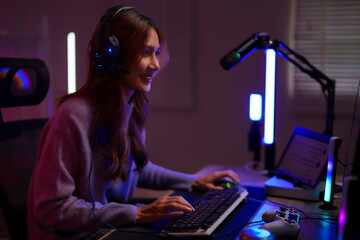 Asian young adult woman gamer streamer plays games online using modern gaming setup technology at home desk room night live stream setup