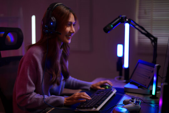 Asian young adult woman gamer streamer plays games online using modern gaming setup technology at home desk room night live stream setup - Powered by Adobe