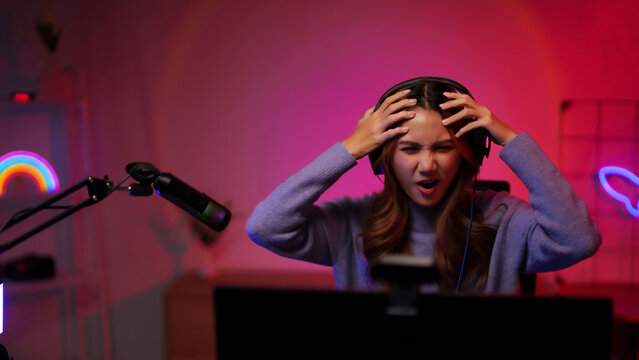 Young adult Asian female streamer reaction intense gaming online video competition esports challenge stress dark neon lit room setup