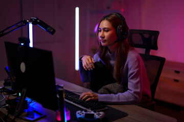 Asian woman professional gamer streaming live video gameplay competition online from dark home studio setup with neon lights
