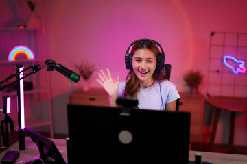 Young Asian adult woman streamer content creator live streaming gaming online home room setup technology neon lights happy smile wave camera