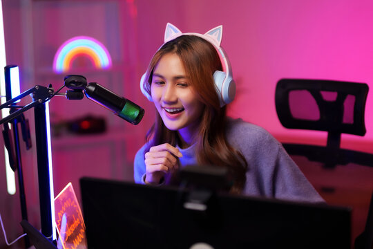 Asian young adult woman streamer live streams games at home studio using technology equipment