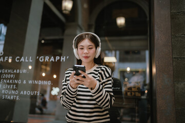 A cheerful young woman with braces wears headphones and smiles while video calling on her...