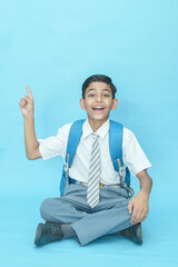 Indian student schoolboy wearing uniform holding notebooks and bag pointing at blank space isolated...