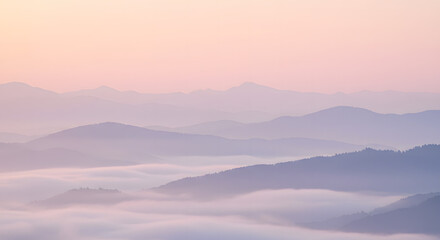 Serene mountain range landscape with layers of soft, hazy peaks and valleys shrouded in mist under a pastel pink and blue sky at dawn.