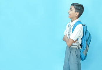 Happy Indian schoolboy student looking at blank space standing isolated over blue background,...