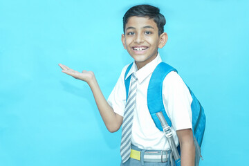 Happy Indian primary schoolboy student pointing at blank space isolated over blue background,...