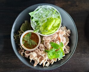 A dish of pork, vegetables and dipping sauce arranged in a beautiful plate.