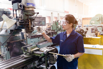 Asian woman industrial engineer in an uniform looking and check old model lathe and drilling machine with clipboard at industrial workshop.