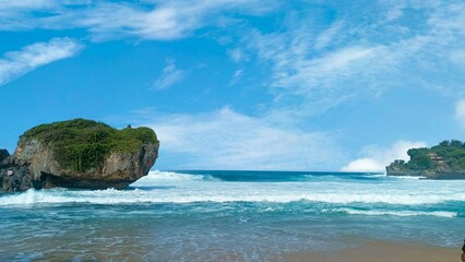 Scenic coastal landscape with large rock, ocean, sky and clouds on a sunny day