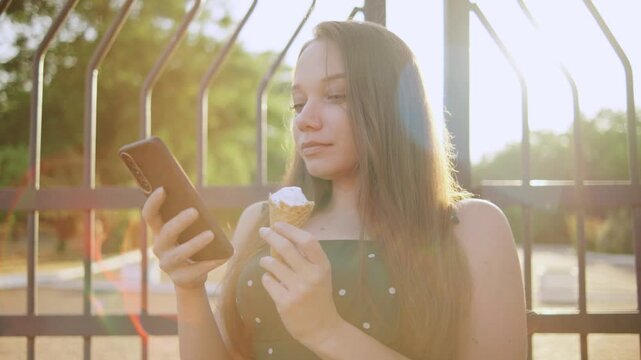 disabled woman in a wheelchair enjoying ice cream while using smartphone in sunny park