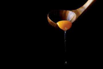 Egg yolk dripping from wooden spoon on black background