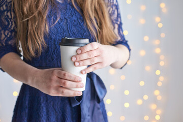 Caucasian female in blue lace dress holding coffee cup with sparkling light background.