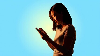 Woman using phone on gradient blue background, silhouetted by warm light
