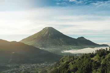 A tranquil mount Sundoro scene featuring a towering peak, dense forests, and a serene village below...