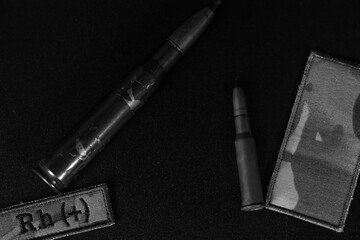 Monochrome military essentials: ammunition and a blood type patch, laid out starkly on a dark...