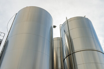 Gros plan de grandes cuves en inox photographiées en extérieur, illustrant leur surface métallique brillante et leur usage industriel.