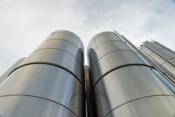 Gros plan de grandes cuves en inox photographiées en extérieur, illustrant leur surface métallique brillante et leur usage industriel.
