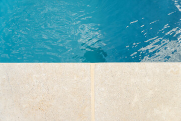 Gros plan sur l’eau cristalline d’une piscine avec aperçu du contour en pierre naturelle,...
