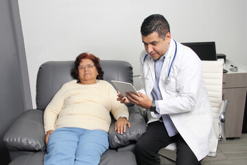 An elderly Latina woman in consultation with a geriatric specialist for a checkup notes her symptoms with the office