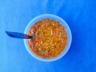 Spicy chili sauce in plastic bowl isolated on blue background