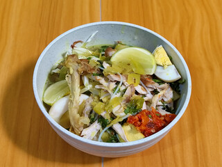 A bowl of Indonesian chicken soto with shredded chicken, sliced boiled egg, vermicelli, sliced...